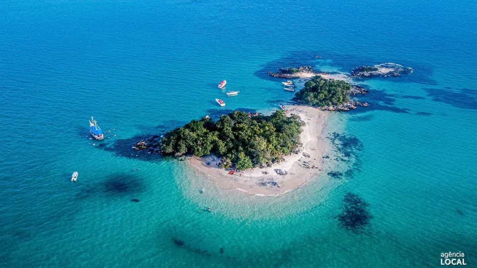 Ilhota com faixa de areia branca e água azul-turquesa, cercada de escuna e lanchas - passeio de lancha na região da Ilha Grande
