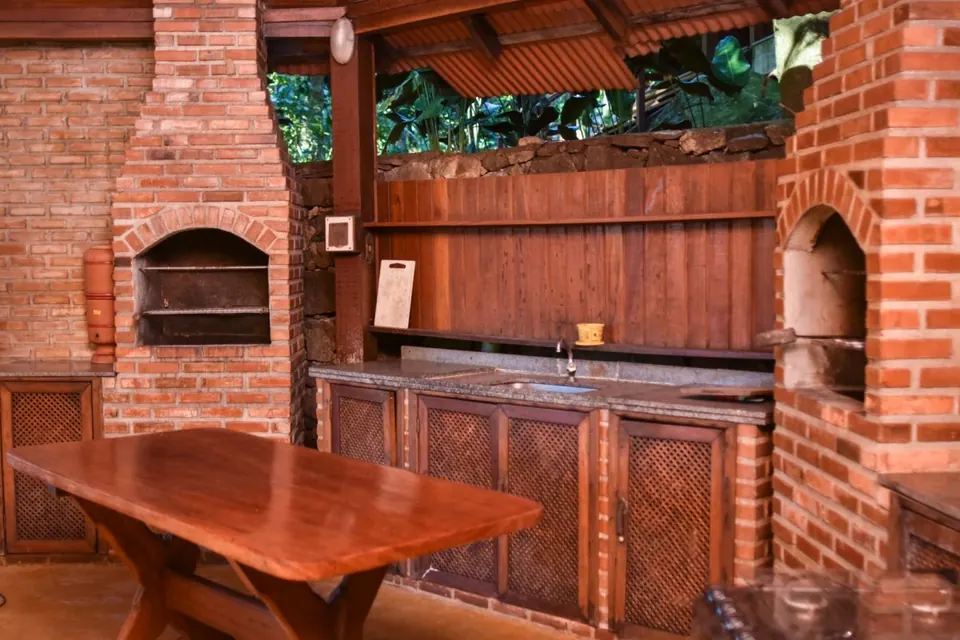 Área de churrasqueira com fornos de tijolo e mesa de madeira da Pousada Mata Nativa